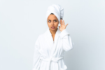 Young woman in bathrobe over isolated white background listening to something by putting hand on the ear