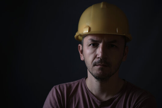 Dirty miner in yellow helmet on dark background. Portrait of face close up.