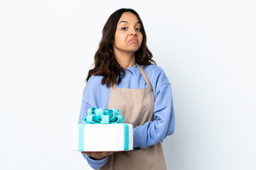 Fototapeta premium Pastry chef holding a big cake over isolated white background making doubts gesture while lifting the shoulders