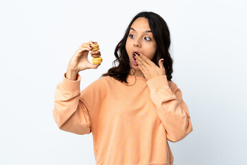Young woman over isolated white background holding colorful French macarons and with surprise expression