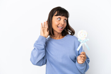 Fototapeta na wymiar Young mixed race woman holding a lollipop isolated on white background listening to something by putting hand on the ear