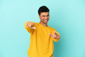 Young African American man isolated on blue background pointing front with happy expression