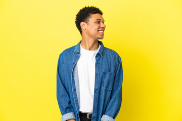 Young African American man isolated on yellow background looking side
