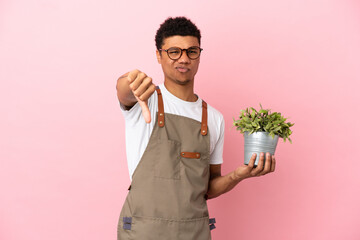 Gardener African man holding a plant isolated on pink background showing thumb down with negative...