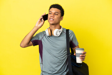 Young sport African American man with sport bag isolated on yellow background holding coffee to take away and a mobile