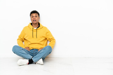 Young African American man sitting on the floor isolated on white background with surprise facial expression