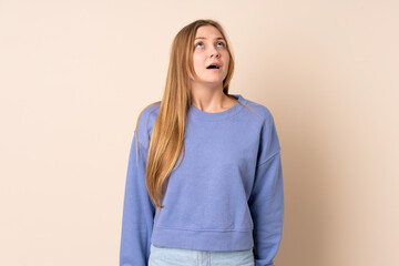 Obraz premium Teenager Ukrainian girl isolated on beige background looking up and with surprised expression