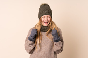 Teenager Ukrainian girl with winter hat isolated on beige background celebrating a victory
