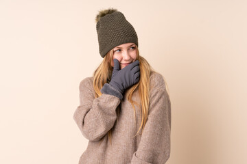 Teenager Ukrainian girl with winter hat isolated on beige background thinking an idea