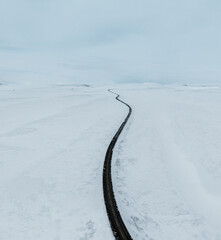 Obraz premium aerial drone view Uphill road landscape in winter at Iceland. Asphalt road with sideways full of snow during winter with blue sky.