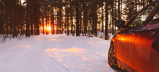 car on a snowy road in the forest at sunset