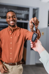 blurred african american car dealer smiling while giving key to customer.