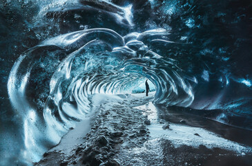 Blue crystal ice cave entrance with tourist climber and an underground river beneath the glacier...