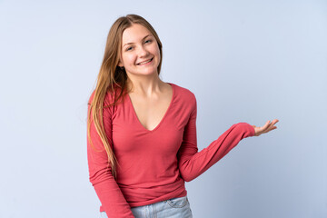 Teenager Ukrainian girl isolated on blue background holding copyspace imaginary on the palm to insert an ad