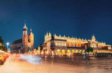 Krakow, Poland. Famous Landmarks On Old Town Square In Summer Evening. St. Mary's Basilica, Cloth Hall Building In Night Lighting. UNESCO World Heritage Site