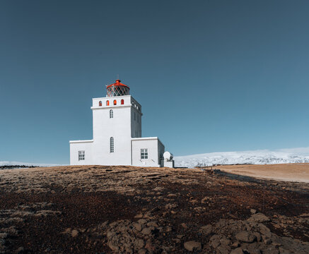 Panoramic image of the lighthouse of Cape Dyrholaey with snow and early morning light with blue sky. winter in Iceland.
