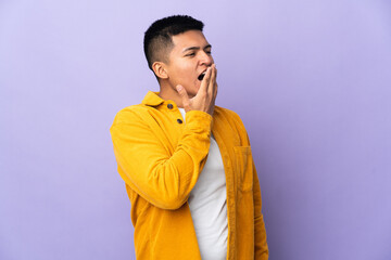 Fototapeta premium Young Ecuadorian man isolated on purple background yawning and covering wide open mouth with hand