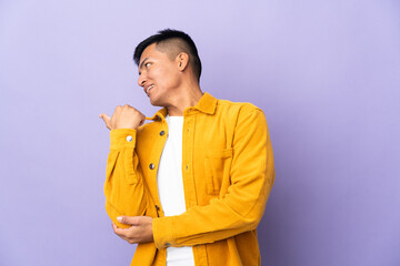 Young Ecuadorian man isolated on purple background pointing to the side to present a product