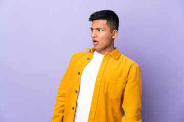 Young Ecuadorian man isolated on purple background doing surprise gesture while looking to the side