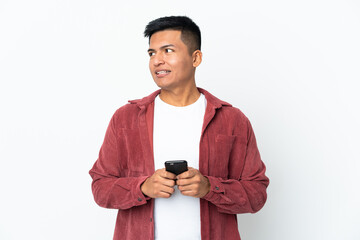 Young Ecuadorian man isolated on white background using mobile phone and looking up