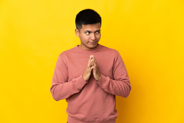 Young Ecuadorian man isolated on yellow background scheming something