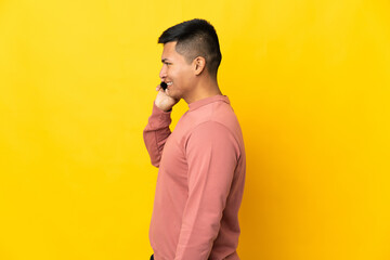 Young Ecuadorian man isolated on yellow background keeping a conversation with the mobile phone with someone