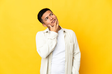 Obraz premium Young Ecuadorian man isolated on yellow background looking up while smiling