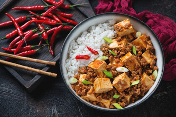 Bowl of chinese traditional mapo tofu and white rice, high angle view on a dark brown stone...