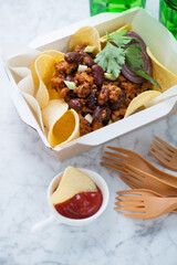Carton takeaway container with mince and bean potato chips, vertical shot on a light-grey marble background, middle close-up