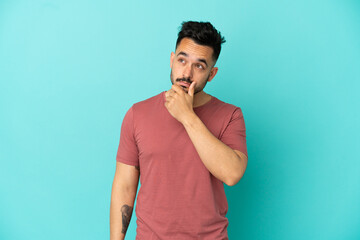 Young caucasian man isolated on blue background having doubts and with confuse face expression