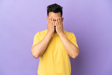 Young caucasian man isolated on purple background covering eyes by hands