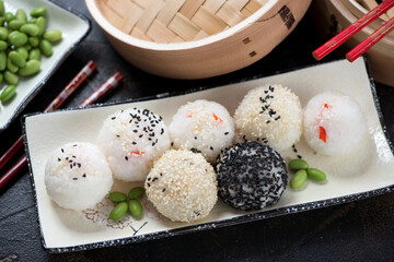 Beige plate with onigiri or japanese rice balls, middle close-up, horizontal shot on a dark brown stone surface