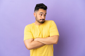Young caucasian man isolated on purple background making doubts gesture while lifting the shoulders