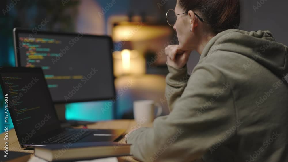 Poster woman in eyglasses and casual wear using laptop and pc for programming at home during evening time. 