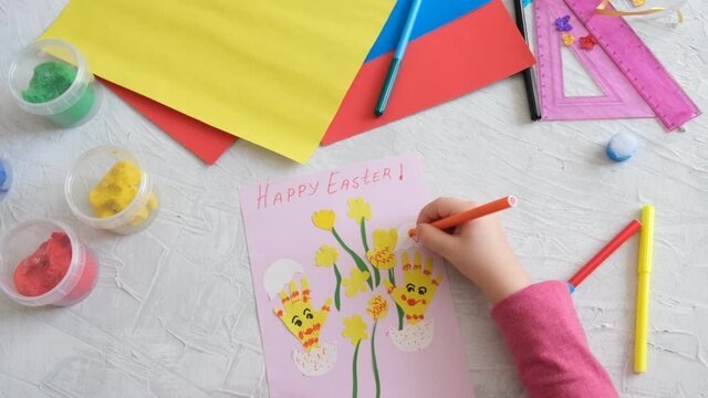 Child making card with Easter funny eggs and flowers  from colorful paper. Handmade. Project of children's creativity, handicrafts, crafts for kids. 