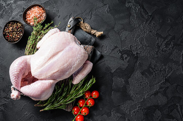 Uncooked raw whole chicken on wooden board with thyme and rosemary. Black background. Top view....