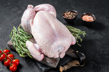 Uncooked raw whole chicken on wooden board with thyme and rosemary. Black background. Top view