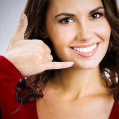 Studio portrait of happy smiling brunette woman showing call me hand sign gesture, over grey color background