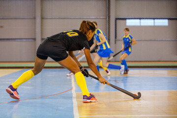 Young woman hockey player playing indoor hockey game
