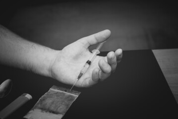 Drug Addict hand with syringe on dark room with a bag of drugs a spoon and a lighter.Toned.