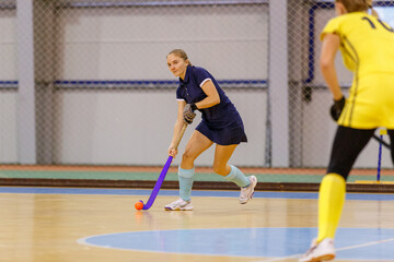 Young woman playing indoor hockey and leading the ball in attack.