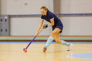 Young woman playing indoor hockey and leading the ball in attack.