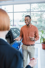 pleased african american man pointing at auto near blurred car dealer.