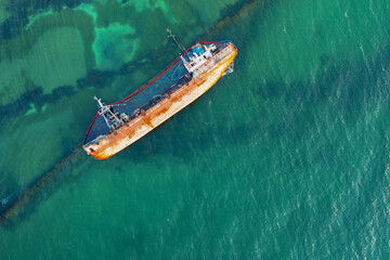 Shipwreck, overturned old rusty barge lying on its side in the water. Drone view.