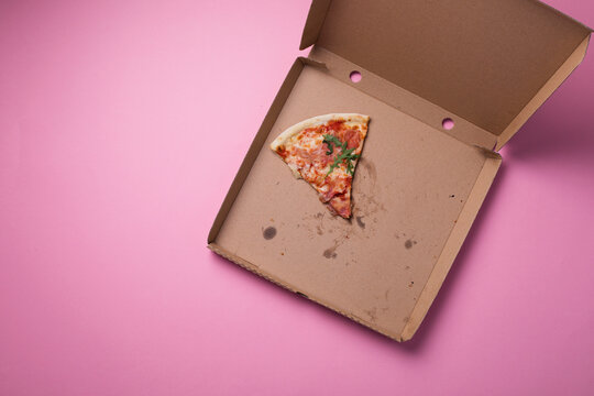 Last slice of pizza, food leftovers on empty pizza cardboard box pink background, top view