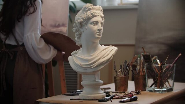 Young woman artist working with a painting - marble bust on the foreground