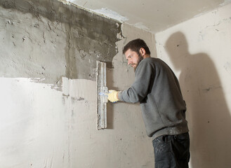 a male plasterer with a beard plasters a concrete wall with a spatula.