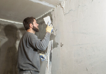 Plakat a male plasterer with a beard plasters a concrete wall with a spatula..