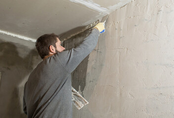 a male plasterer with a beard plasters a concrete wall with a spatula..