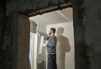 a male plasterer with a beard plasters a concrete wall with a spatula..